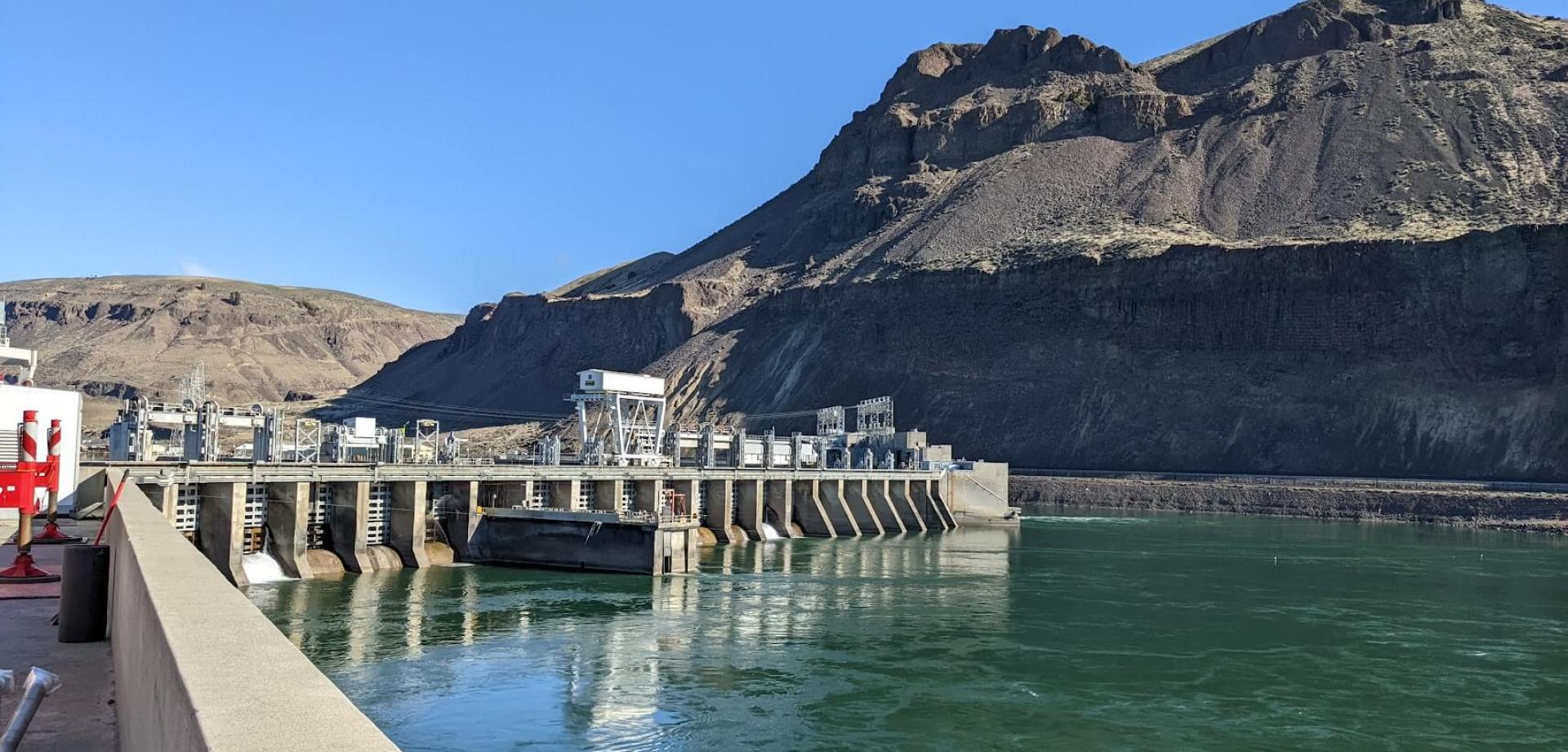 Downstream view of hydroelectric dam and powerhouse with large hoist actuated water control gates.