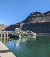 Downstream view of hydroelectric dam and powerhouse with large hoist actuated water control gates.