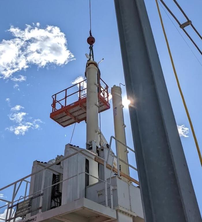 Mechanic in a man basket suspended by a crane making final connections to a long stroke hydraulic cylinders being installed at a dam.